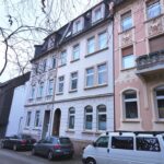 Häuserfronten mit dem Mehrfamilienhaus in Iserlohn. Vor dem Haus parken Autos. Die Straße ist verkehrsberuhigt.