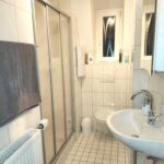 Badezimmer in der Dachgeschoßwohnung des Mehrfamilienhauses mit Waschtisch, Dusche und WC.