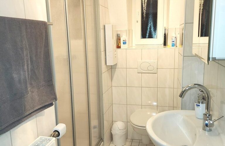 Badezimmer in der Dachgeschoßwohnung des Mehrfamilienhauses mit Waschtisch, Dusche und WC.