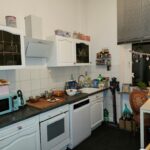 Die Küche im Erdgeschoß mit weißen Einbaumöbeln. Die Wände sind weiß. Das Fenster hat ein Rollo.