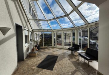 Repräsentatives Eingangsportal zu den Büroflächen in Iserlohn. Ausgestattet Mit bequemen Sitzmöbeln und einem Glaskuppel-Dach. Man kann dieses Büro in Iserlohn mieten.