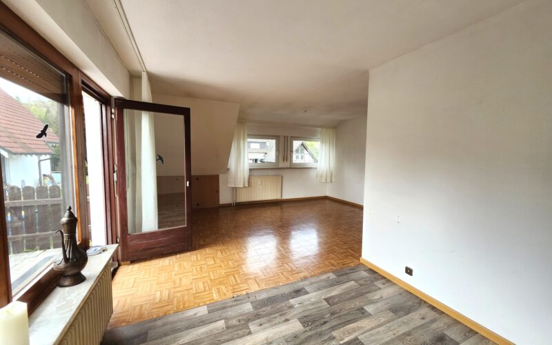 Blick durch das Wohnzimmer vom Balkon aus. Das Wohnzimmer hat unterschiedliche Fußbodenbeläge