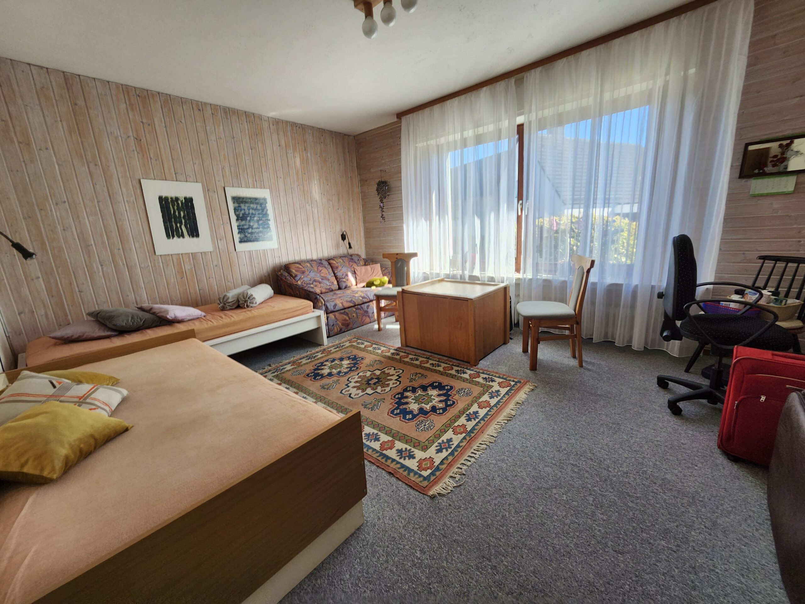 Zimmer im Erdgeschoß mit Teppichboden und großem Fenster.