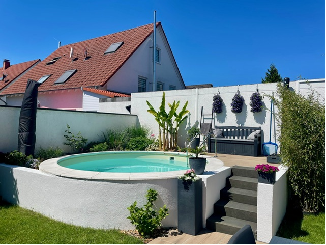 Poolanlage im Garten des Einfamilienhauses mit Treppe und erhabener Terrasse im Sonnenschein