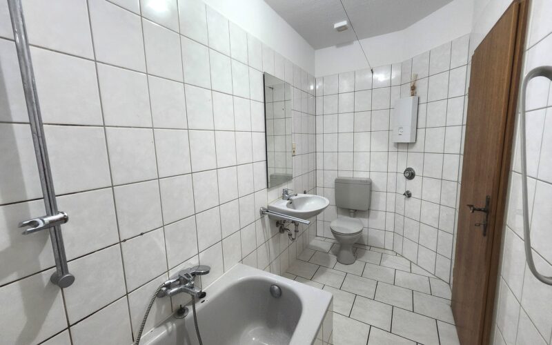 Bad mit Blick von der Wanne aus. Das Bad ist grau gefliest. Es gehört zur Mietwohnung im ersten Obergeschoß
